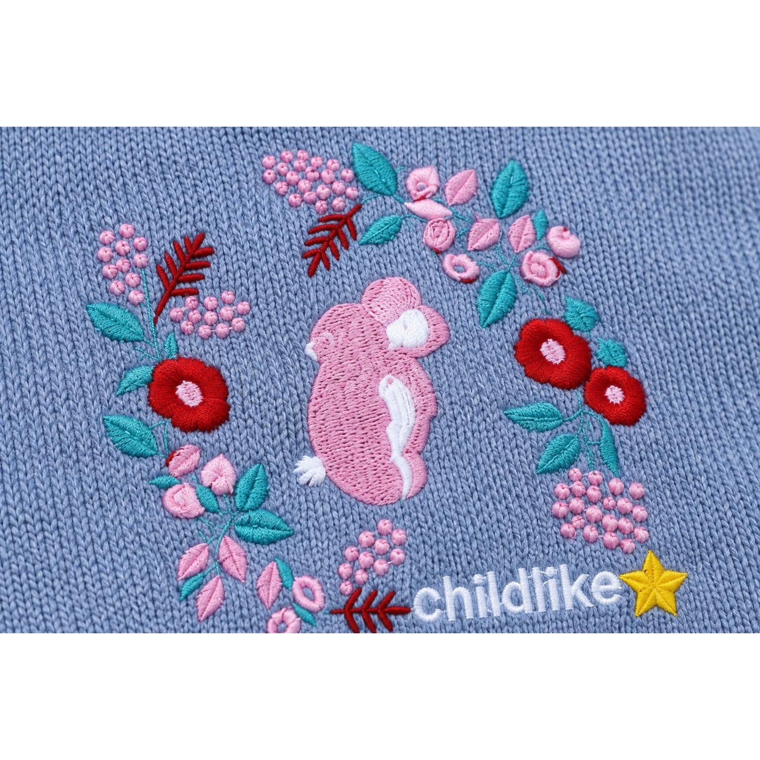Pink rabbit surrounded by embroidered pink and red flowers and green leaves on the grey-blue knitted sweater.